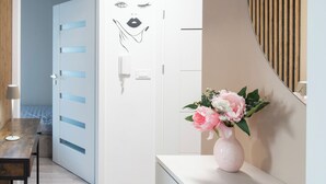 Ein Zimmer mit einem Bett, einem Schreibtisch, einer weißen Tür mit blauem Feld, einer Wandleuchte und einer Vase mit Blumen.