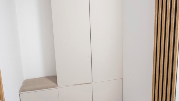 Ein weißer Kleiderschrank mit Sitzbank und einer Trennwand aus Holzleisten.