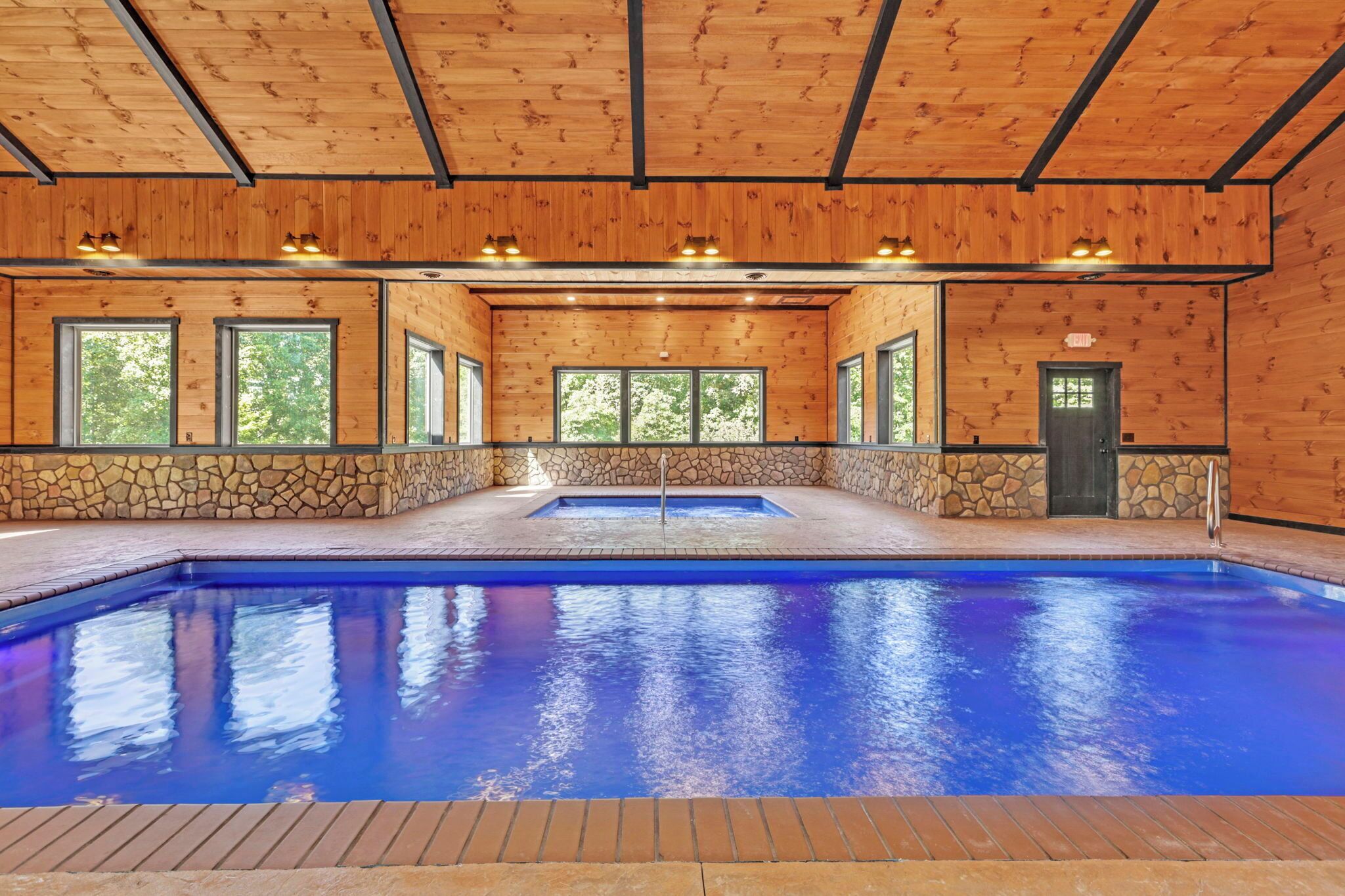 A swimming pool with a stone wall and wooden ceiling, surrounded by windows.