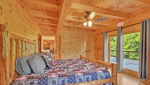 Ein Schlafzimmer einer Holzhütte mit Bett, Deckenventilator und Blick ins Freie.