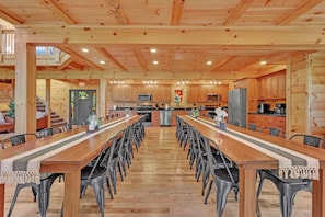 A spacious dining area with a long wooden table and chairs, a kitchen with wooden cabinets, and a staircase leading to an upper level. - NEW! Jenny Lynn Lodge (Logan)