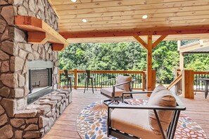An outdoor patio with a stone fireplace, wooden deck, and outdoor seating. - NEW! Jenny Lynn Lodge (Logan)