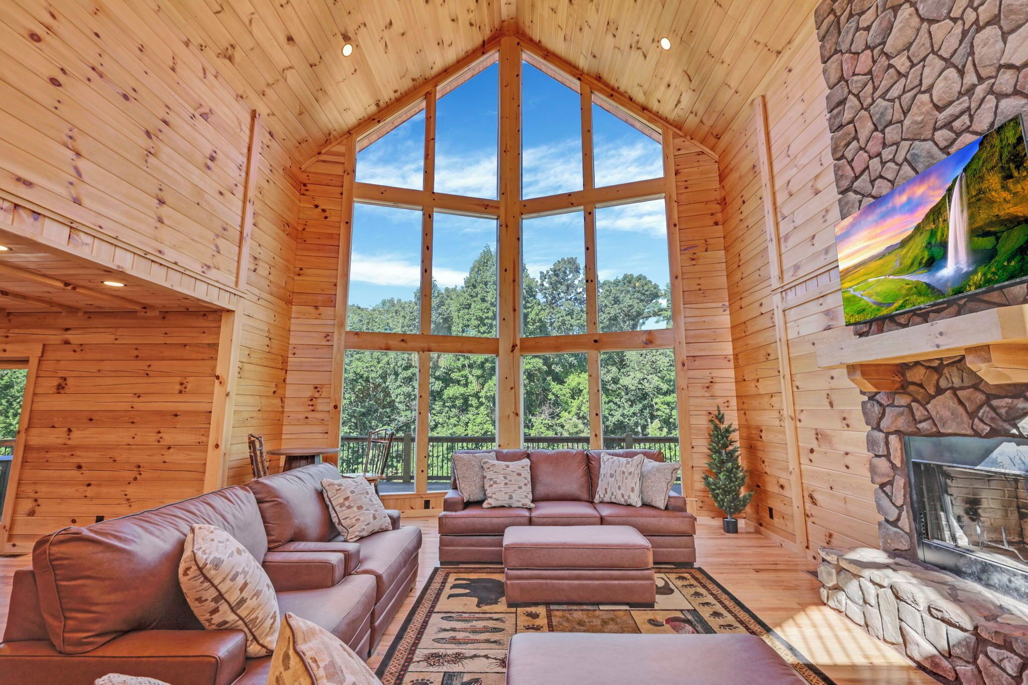 L’intérieur d’une cabane en rondins, avec une grande fenêtre, une cheminée et un coin salon confortable.