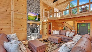 Ein großzügiges Wohnzimmer mit Kamin aus Naturstein, Ledersofas und einem großen Fenster mit Blick auf eine malerische Landschaft.