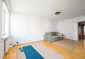 Habitació amb sòl de fusta, un tapet de gimnàstica blau, un sofà gris i una taula petita.