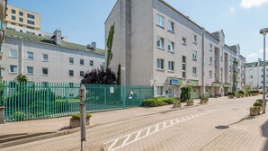 Ein mehrgeschossiges Gebäude mit einer flachen Fassade, einem grünen Zaun und blauem Himmel.
