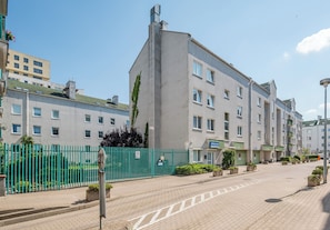 A multi-story building with a flat facade, a green fence, and a clear sky. - Metro Stokłosy Homely Apartment (Warszawa)