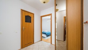 Ein Flur mit einer Holztür, einem Spiegel und Blick in ein Schlafzimmer mit einem Bett und einer blauen Decke.