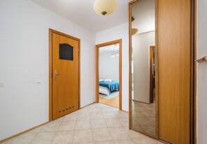 A hallway with a wooden door, a mirror, and a view into a bedroom with a bed and a blue blanket. - Metro Stokłosy Homely Apartment (Warszawa)