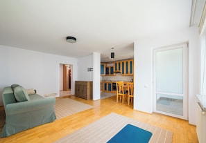 A modern living room with a sofa, a dining table with chairs, and a kitchen area with wooden cabinets. - Metro Stokłosy Homely Apartment (Warszawa)