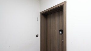 Une porte en bois fermée, dotée d’une petite serrure électronique, un interrupteur fixé au mur et le numéro de porte « 82 » sur le mur adjacent.
