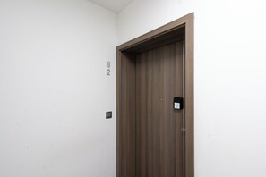 Eine geschlossene Holztür mit einem kleinen elektronischen Schloss, einem an der Wand montierten Lichtschalter und der Türnummer '82' in der angrenzenden Wand.