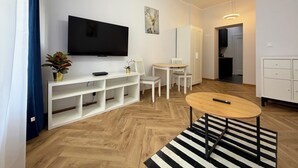 Ein modernes Wohnzimmer mit Flachbildfernseher, weißen Möbeln, einem Streifenmuster-Teppich und Holzboden.