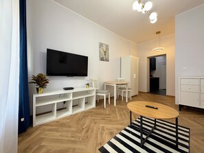 Ein modernes Wohnzimmer mit Flachbildfernseher, weißen Möbeln, einem Streifenmuster-Teppich und Holzboden.