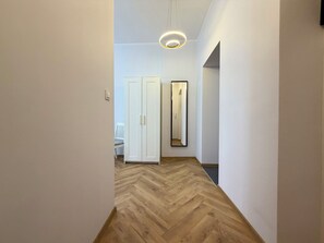 Ein Korridor mit Holzdielen im Fischgrätmuster, weißen Wänden, einer weißen Tür und einem Spiegel, der eine Tür und einen Stuhl reflektiert.