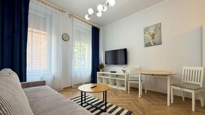 Ein Wohnzimmer mit einer Couch, einem Esstisch mit Stühlen, einem Fernseher und einer Uhr an der Wand.