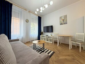 Ein Wohnzimmer mit einer Couch, einem Esstisch mit Stühlen, einem Fernseher und einer Uhr an der Wand.