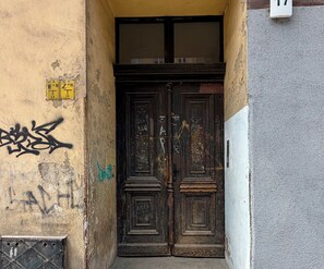 A dark wooden double door with visible wear and graffiti, set in a narrow alleyway with peeling paint and a metal grate. - Prądzyńskiego Downtown Studio (Wrocław)