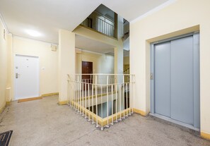 Ein mehrgeschossiges Interieur mit einer Treppe, einer Tür mit der Beschriftung '14' und einem grauen Aufzug.