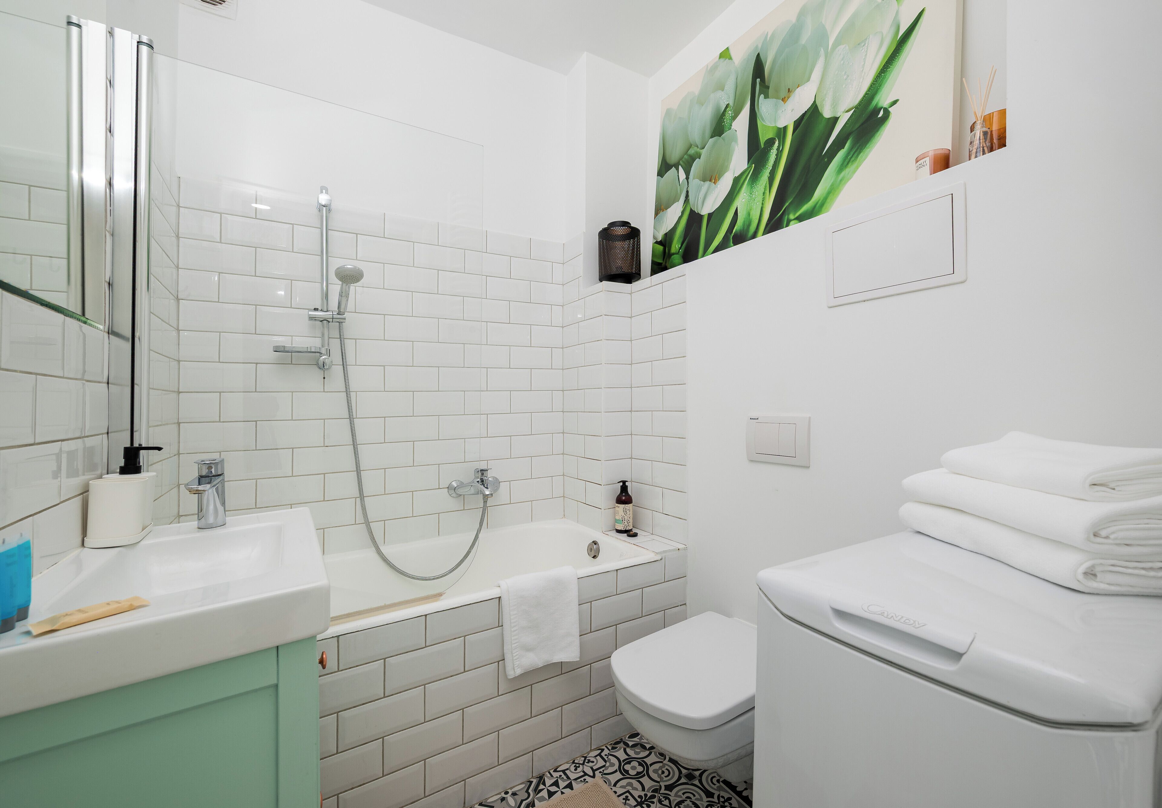 Een badkamer met douche, toilet, wastafel en een bloemschilderij aan de muur.