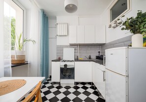 Una cocina compacta con piso a cuadros, gabinetes blancos, estufa y refrigerador.