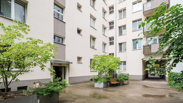 A courtyard with a bench, planters, and a building with multiple windows and balconies. - 3 Maja Cozy Apartment (Warszawa)