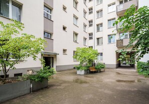 A courtyard with a bench, planters, and a building with multiple windows and balconies. - 3 Maja Cozy Apartment (Warszawa)