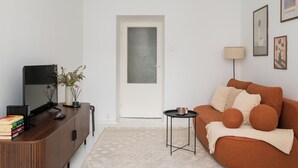 A modern living room with a television, books, a small table, a sofa, and a door. - 3 Maja Cozy Apartment (Warszawa)