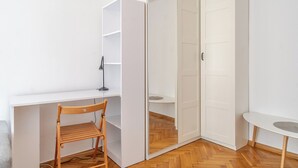 Quarto com uma cadeira de madeira, uma escrivaninha e um guarda-roupa branco.
