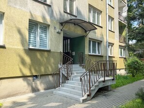 A multi-story building with a staircase leading to the entrance, metal railings, and a small window with shutters. - Grabowa Harmony Studio (Katowice)