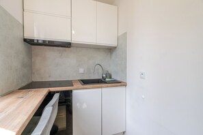 A compact kitchen with white cabinets, a stainless steel range hood, a sink with a faucet, and a wooden countertop. - Grabowa Harmony Studio (Katowice)