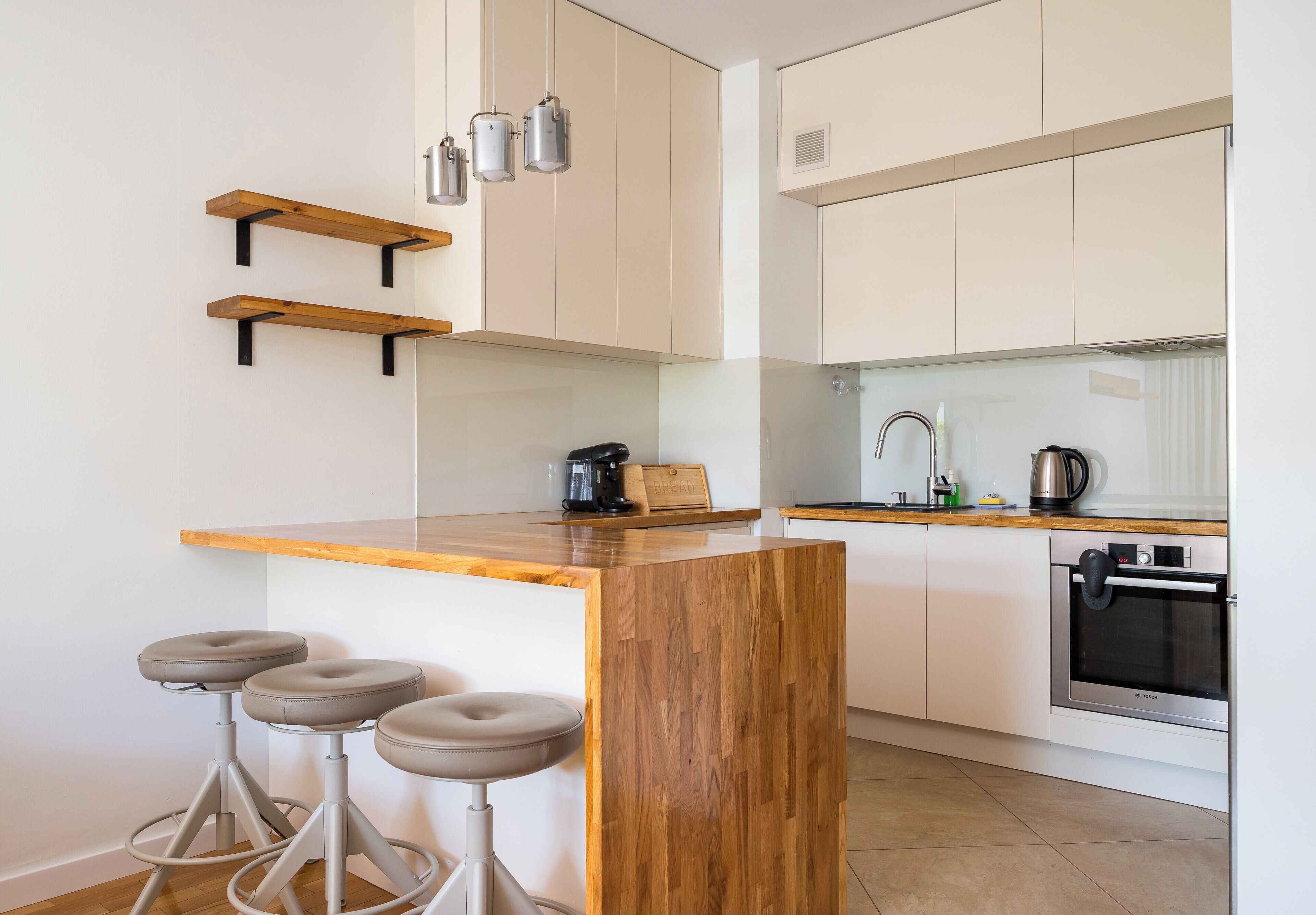 Una cocina moderna con taburetes de madera, electrodomésticos de acero inoxidable y armarios blancos.