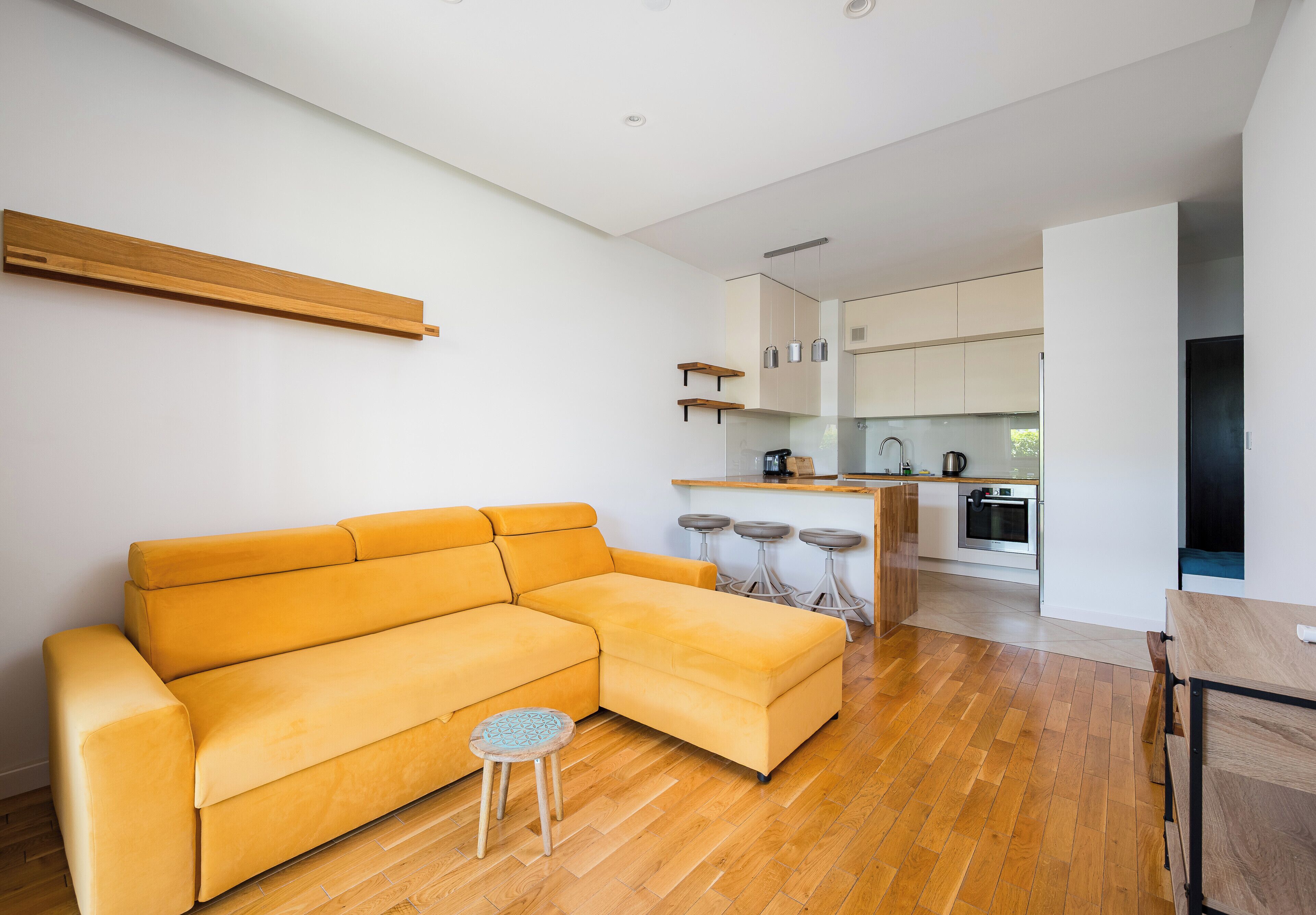 Een moderne woonkamer met een bank, een klein krukje en een keuken in de achtergrond.