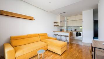 Een moderne woonkamer met een bank, een klein krukje en een keuken in de achtergrond.