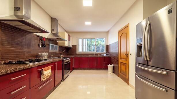 A modern kitchen with stainless steel appliances, red cabinetry, and a window providing natural light. - Exceptional Villa with Pool, Jacuzzi, and Sauna—2 Minutes from the Beach (Dar Bouazza)