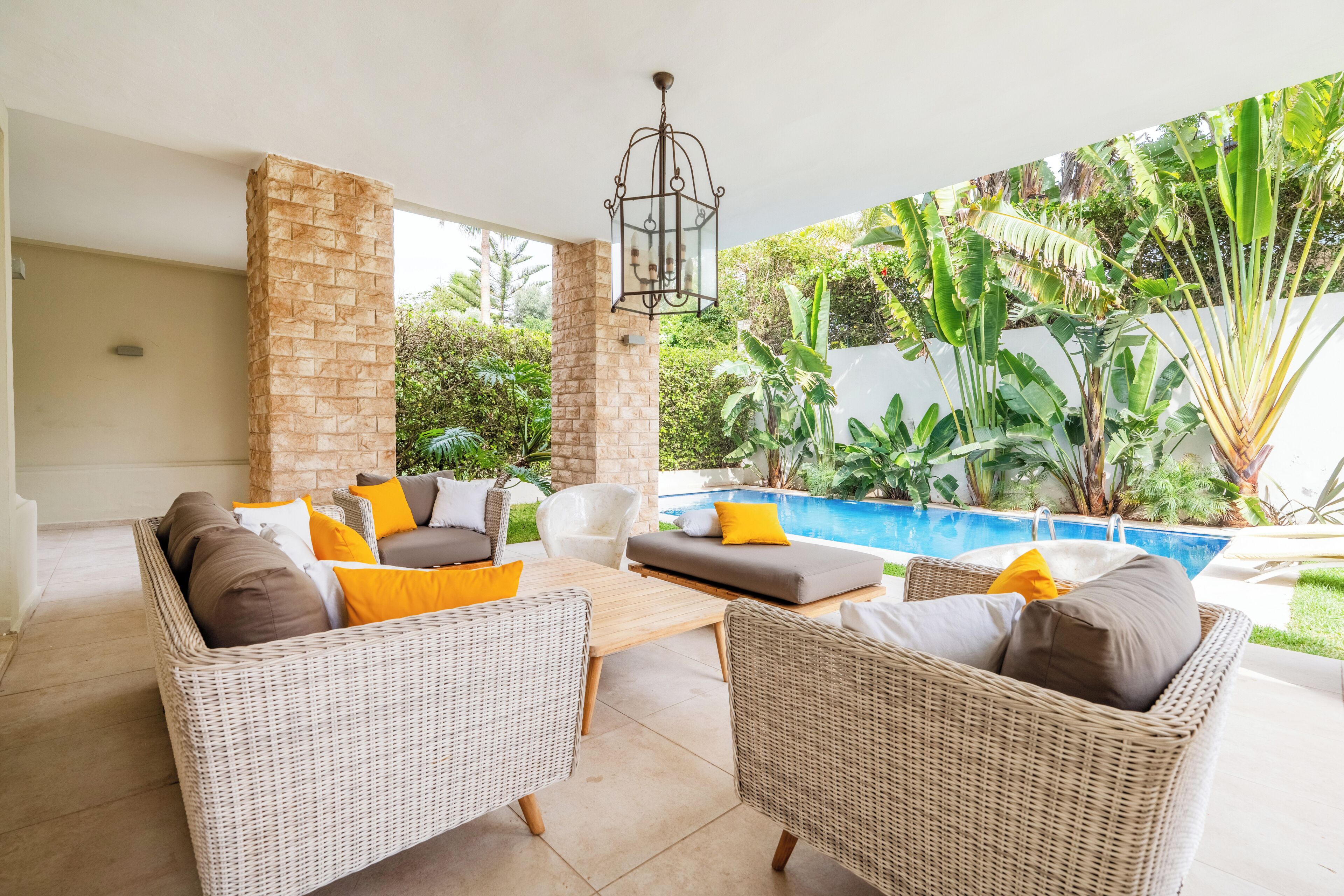 Un patio con mobiliario de mimbre, una piscina y abundante vegetación.