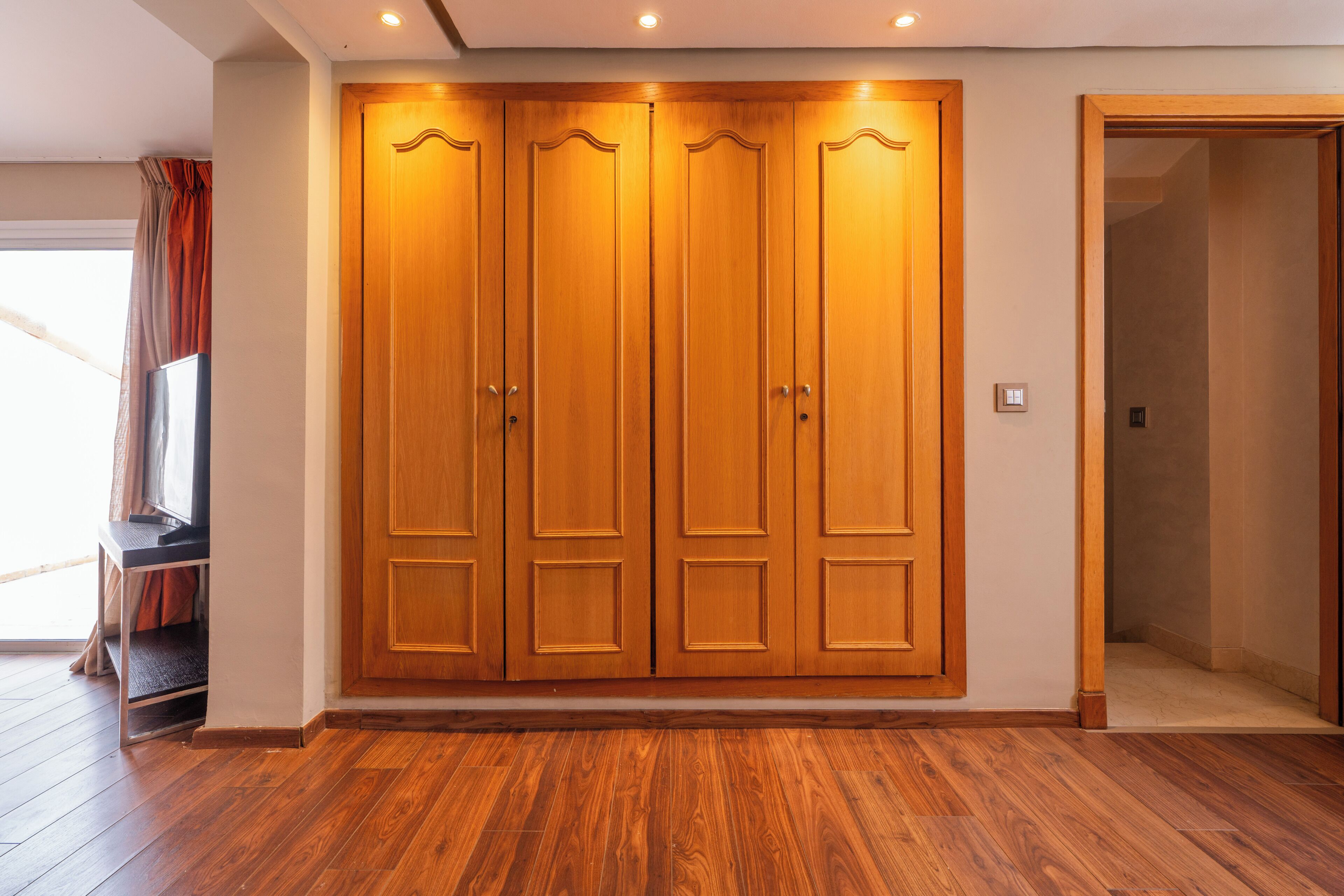 Una habitación con un armario de madera, televisor y una puerta que da a otra estancia.