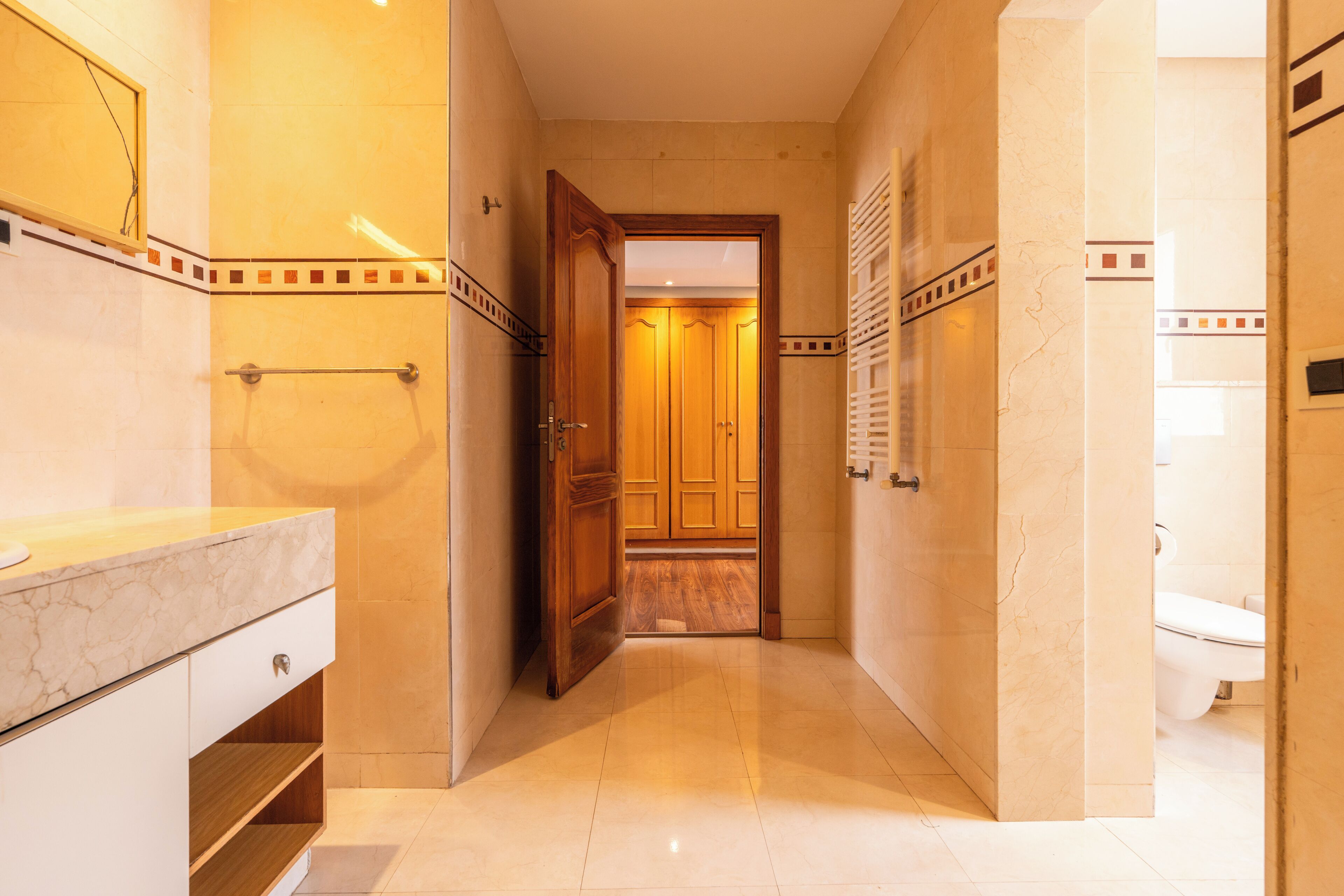 Une salle de bain d’hôtel avec un lavabo en marbre, un porte-serviettes et une porte en bois donnant accès à une cabine de douche.