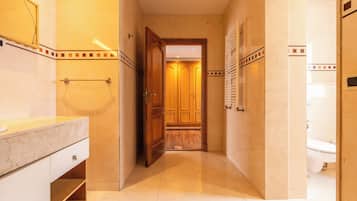 Une salle de bain d’hôtel avec un lavabo en marbre, un porte-serviettes et une porte en bois donnant accès à une cabine de douche.