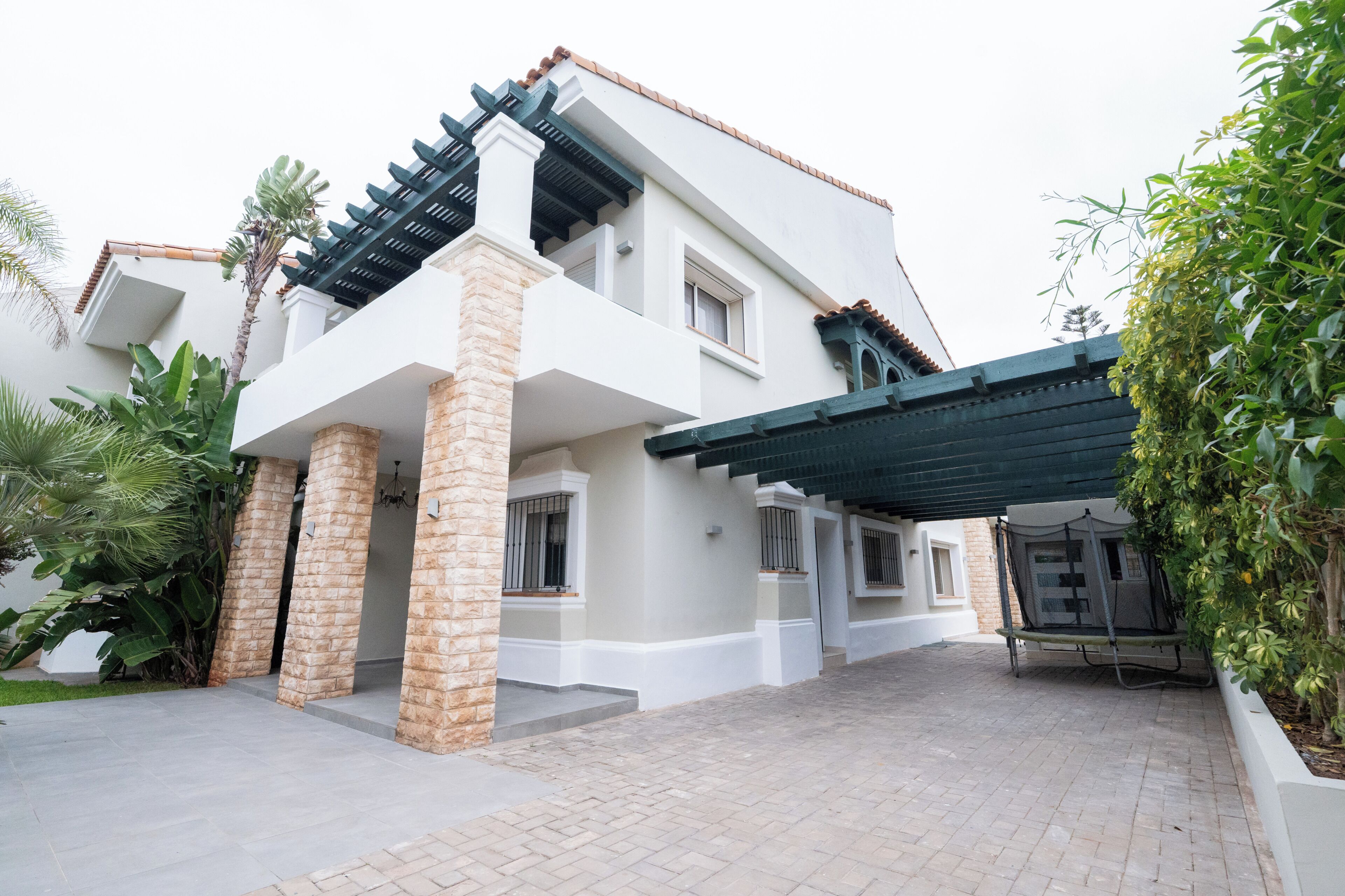 A two-story house with a covered patio area, stone pillars, and a tiled entrance.