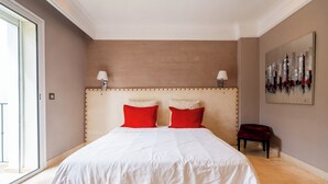 A large bed with a beige headboard and red pillows, a small bedside table with a lamp, and a painting on the wall. - Exceptional Villa with Pool, Jacuzzi, and Sauna—2 Minutes from the Beach (Dar Bouazza)