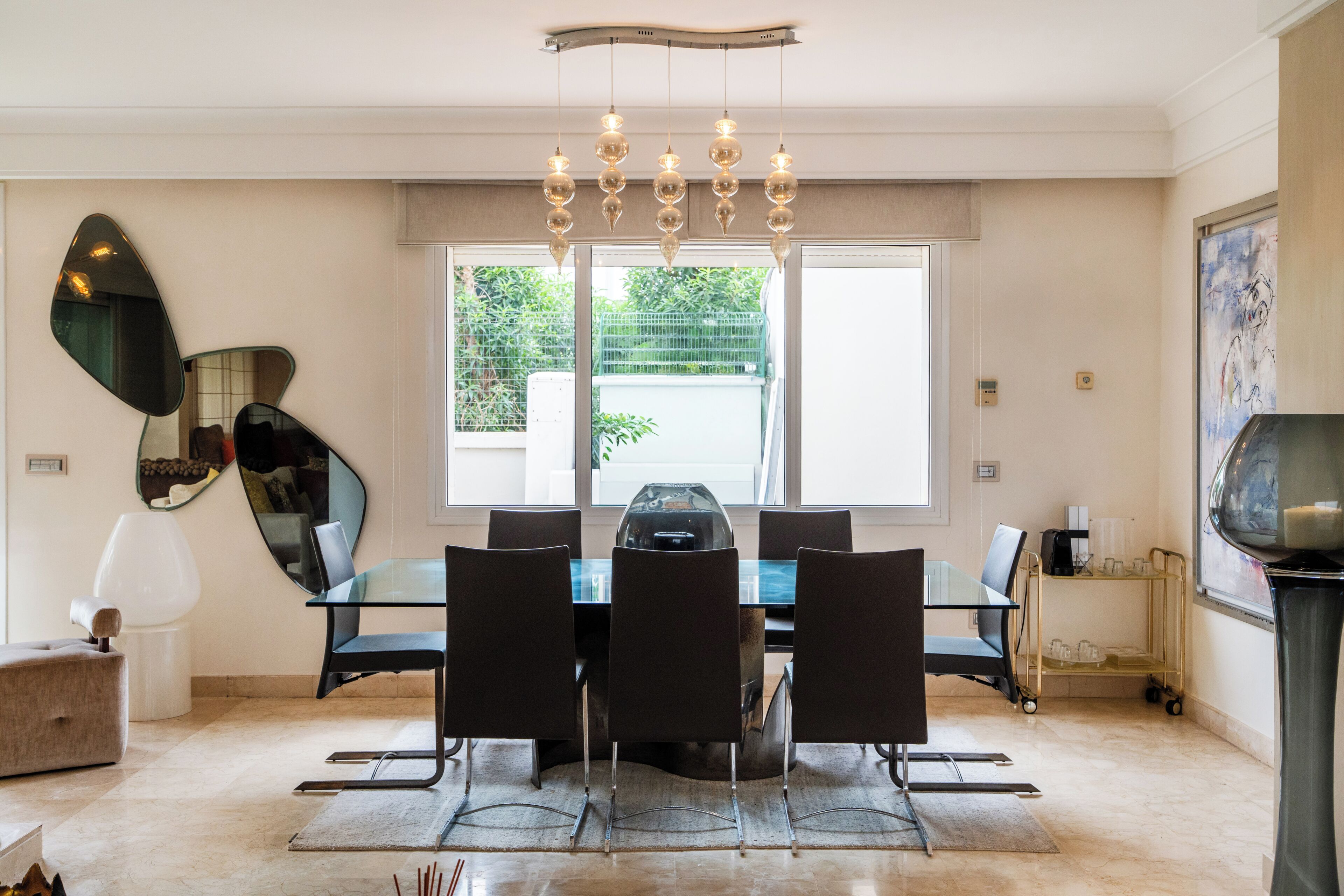 Un comedor moderno con una mesa de vidrio, sillas negras y una lámpara original.