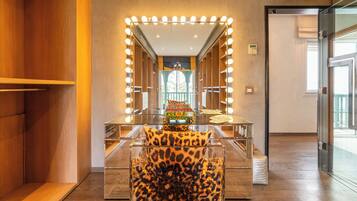 Una stanza con uno specchio da toilette illuminato, una poltrona con stampa leopardata e un tavolino in vetro con oggetti decorativi.