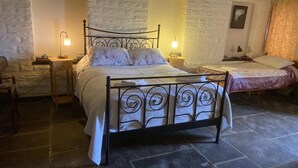Una habitación con una cama de estructura metálica, dos mesitas de noche con lámparas, una pared de piedra y un edredón estampado con motivos florales.