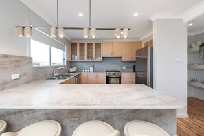 A modern kitchen with a marble countertop, stainless steel appliances, and a central island with seating. - Mollymere | Ocean View Coastal Retreat (Mollymook Beach)