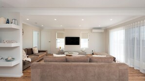 Una sala de estar moderna con un amplio sofá seccional color beige, una pequeña mesa redonda de centro y un televisor de pantalla plana montado en la pared.