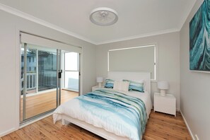A bedroom with a bed, a sliding glass door to a balcony, a ceiling fan, and a painting on the wall. - Mollymere | Ocean View Coastal Retreat (Mollymook Beach)