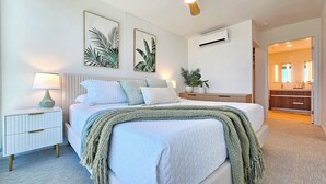Una camera da letto con un letto, comodini, una lampada, opere d'arte alle pareti e vista sul bagno.