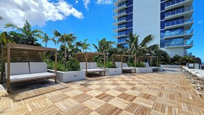 Eine Dachterrasse mit Holzboden, weißen Lounge-Sesseln und Palmen.