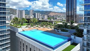 Ein Pool auf dem Dach mit Liegestühlen, umgeben von Grünflächen und modernen Gebäuden.